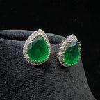 Pair of teardrop green stone and diamond halo earrings displayed on a black stand.