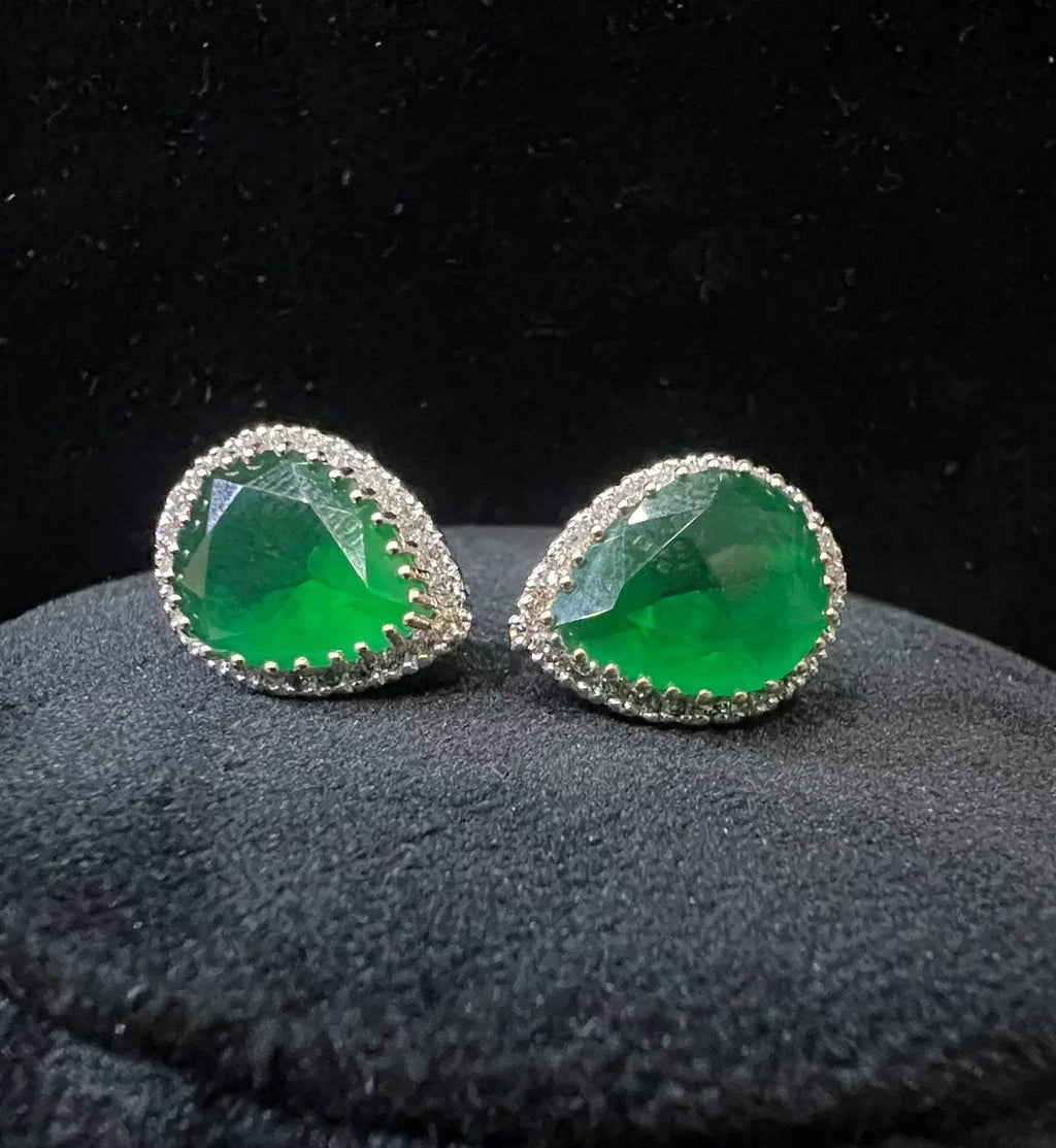 Pair of teardrop green stone and diamond halo earrings displayed on a black stand.