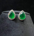 Pair of teardrop green stone and diamond halo earrings displayed on a black stand.
