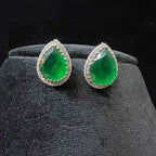 Pair of teardrop green stone and diamond halo earrings displayed on a black stand.