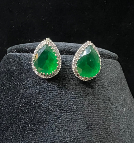 Pair of teardrop green stone and diamond halo earrings displayed on a black stand.
