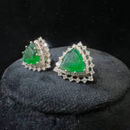 A pair of gold diamond earrings with a green color stone set in a minimalist design on a black background.