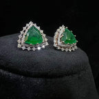 A pair of gold diamond earrings with a green color stone set in a minimalist design on a black background.
