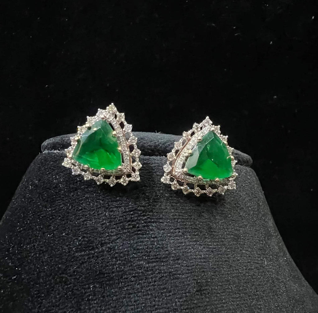 A pair of gold diamond earrings with a green color stone set in a minimalist design on a black background.