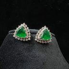 A pair of gold diamond earrings with a green color stone set in a minimalist design on a black background.