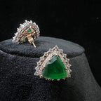 A pair of gold diamond earrings with a green color stone set in a minimalist design on a black background.