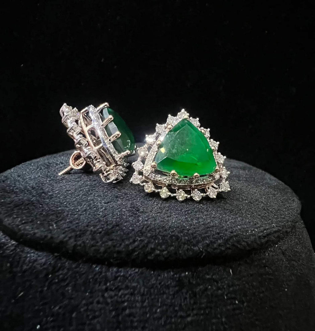 A pair of gold diamond earrings with a green color stone set in a minimalist design on a black background.