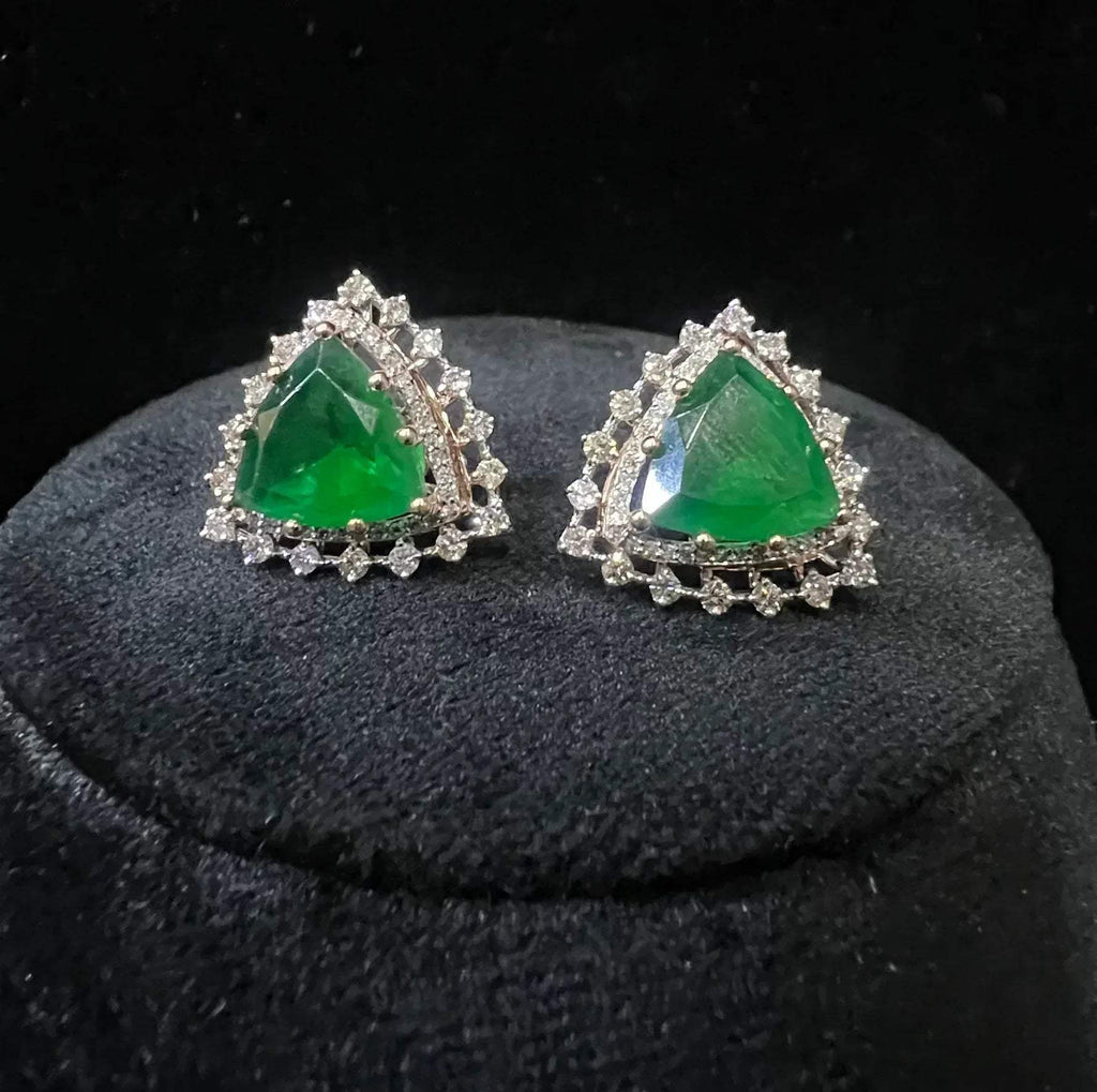 A pair of gold diamond earrings with a green color stone set in a minimalist design on a black background.