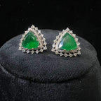 A pair of gold diamond earrings with a green color stone set in a minimalist design on a black background.