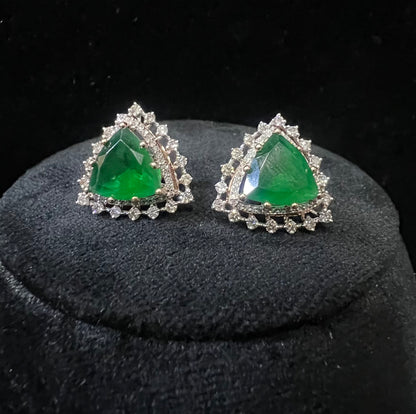 A pair of gold diamond earrings with a green color stone set in a minimalist design on a black background.