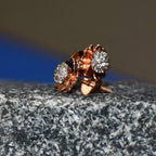 A pair of gold diamond earrings with a brilliant cut design, displayed a stone surface.