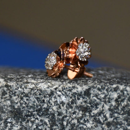 A pair of gold diamond earrings with a brilliant cut design, displayed a stone surface.