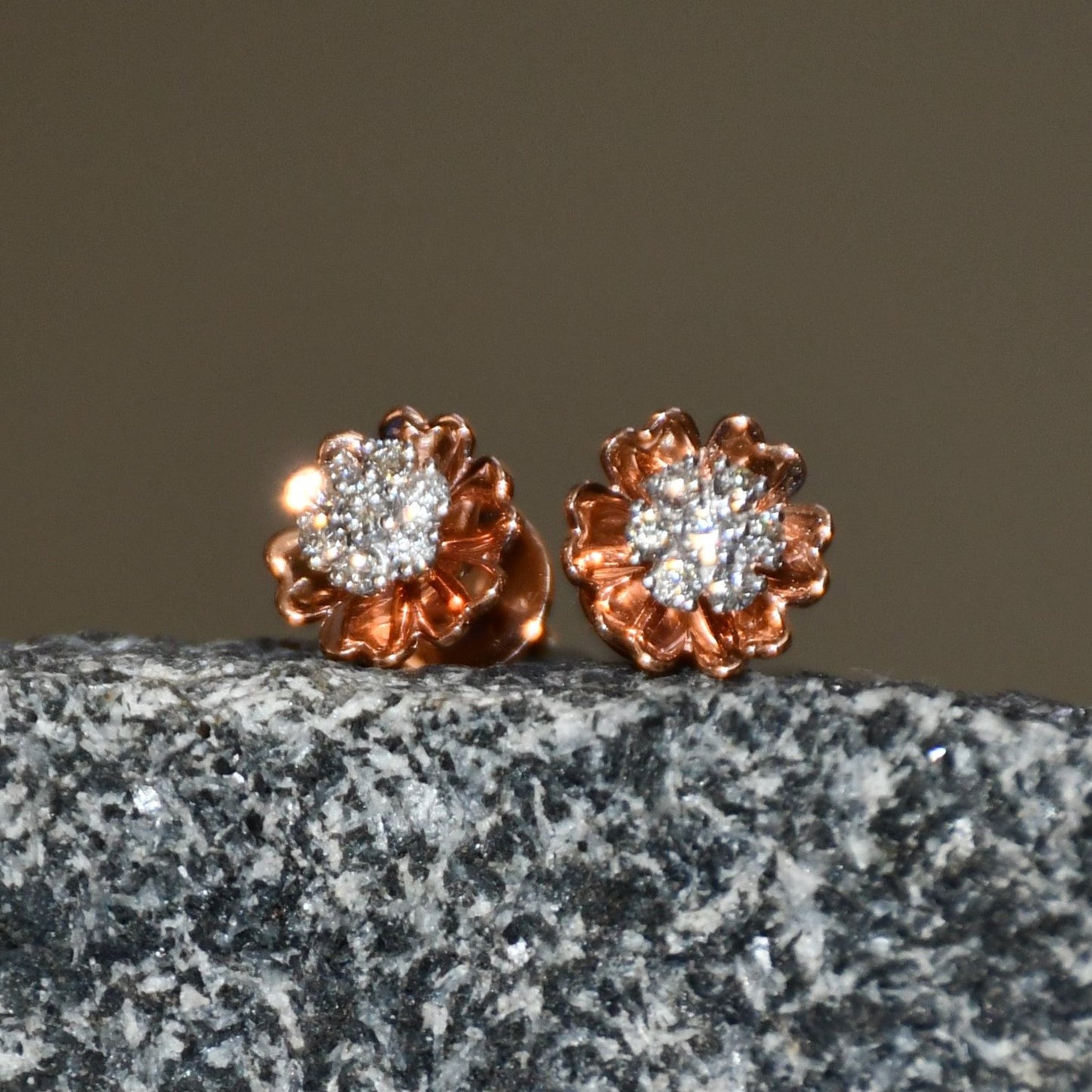 A pair of gold diamond earrings with a brilliant cut design, displayed a stone surface.