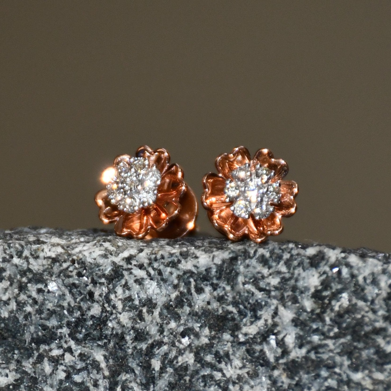A pair of gold diamond earrings with a brilliant cut design, displayed a stone surface.