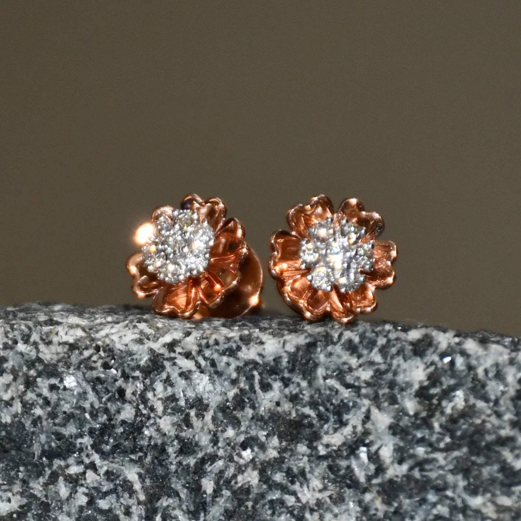 A pair of gold diamond earrings with a brilliant cut design, displayed a stone surface.