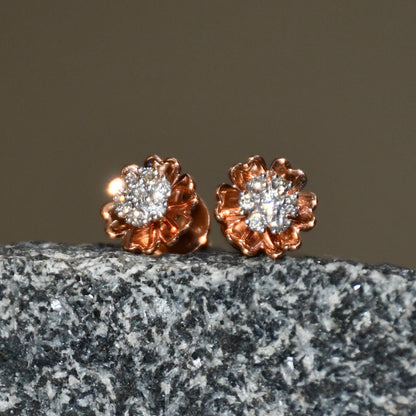 A pair of gold diamond earrings with a brilliant cut design, displayed a stone surface.
