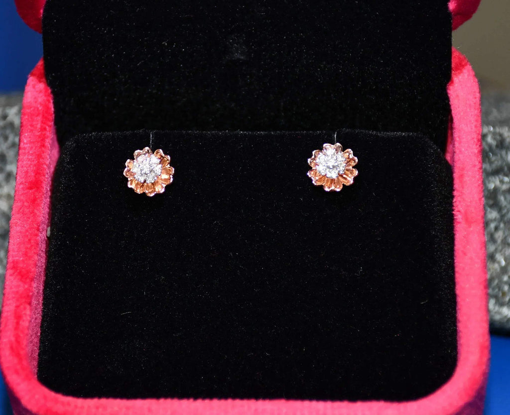 A pair of gold diamond earrings with a brilliant cut design, displayed in a jewelry box.