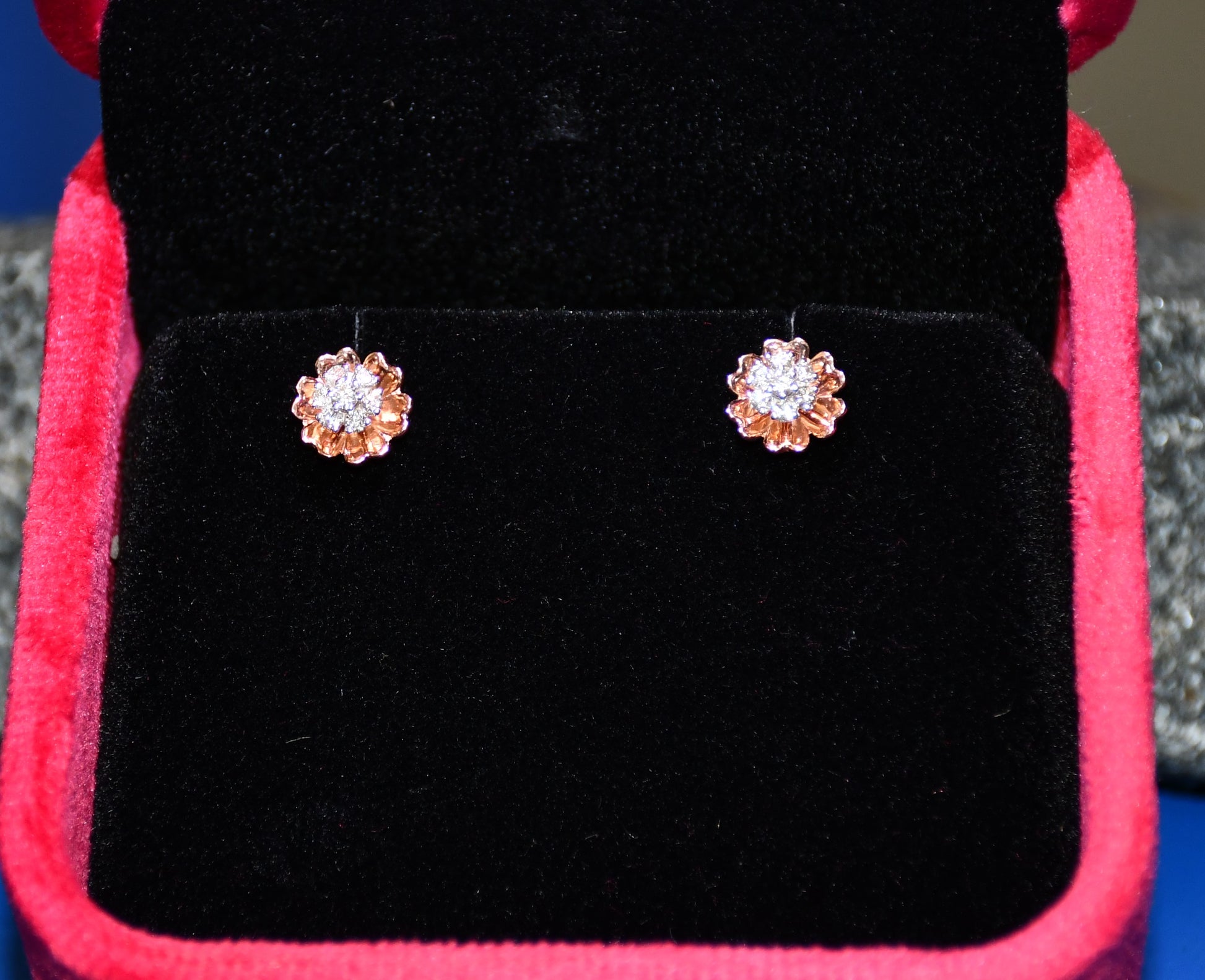 A pair of gold diamond earrings with a brilliant cut design, displayed in a jewelry box.