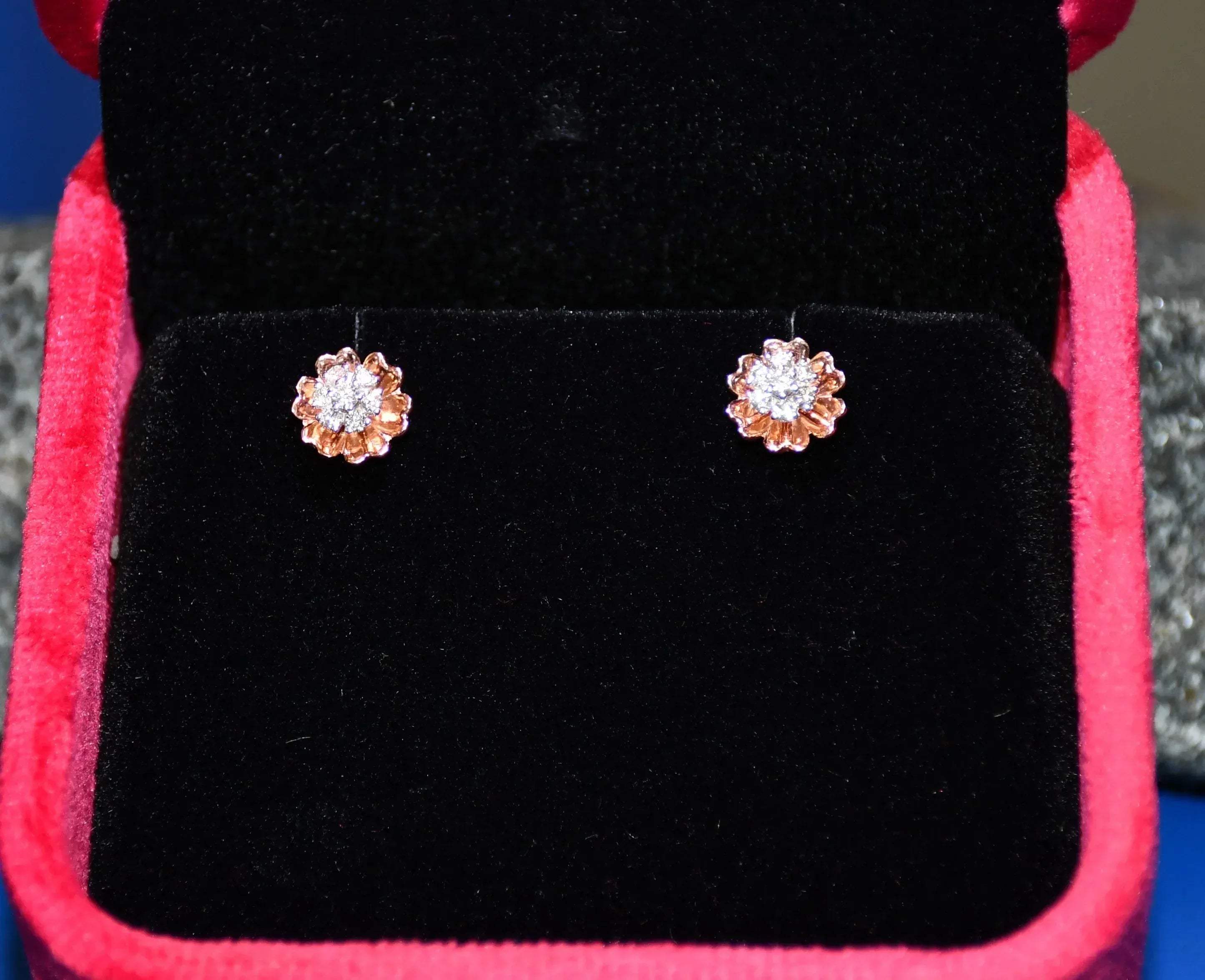 A pair of gold diamond earrings with a brilliant cut design, displayed in a jewelry box.