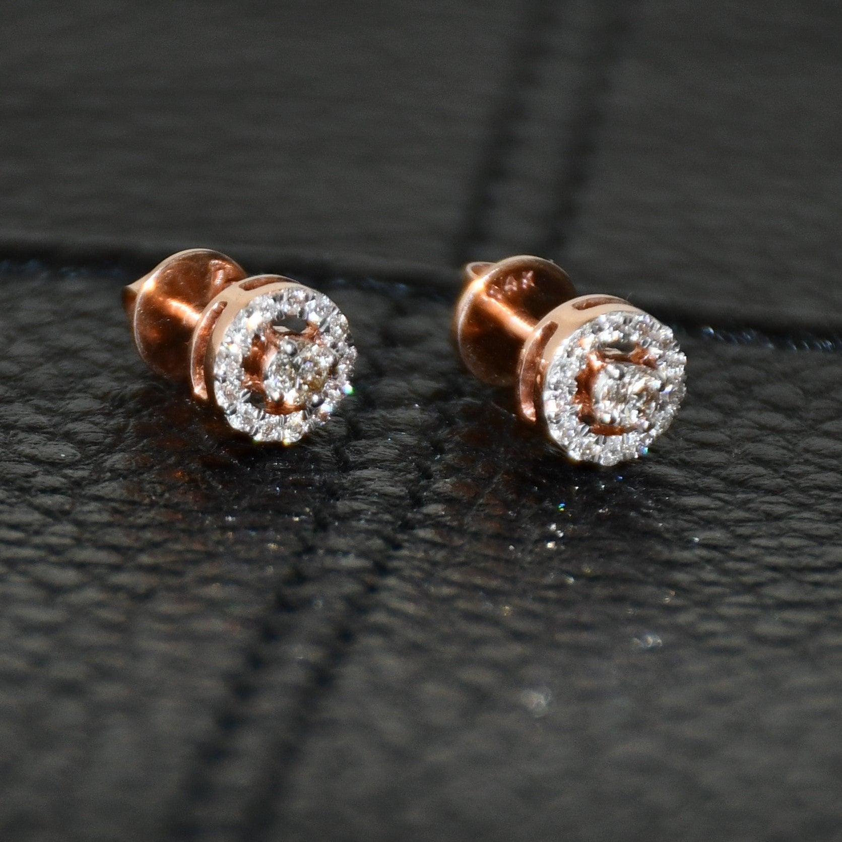 Pair of round halo cluster diamond earrings in gold with center diamonds and surrounding diamond halo, placed on a black surface.