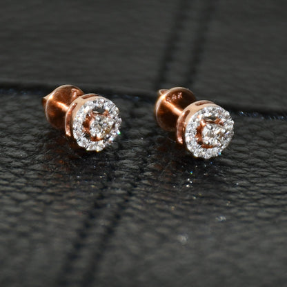 Pair of round halo cluster diamond earrings in gold with center diamonds and surrounding diamond halo, placed on a black surface.