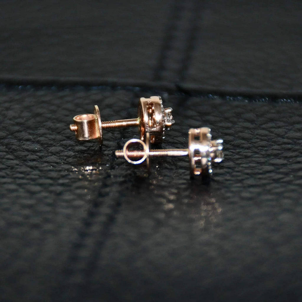 Pair of round halo cluster diamond earrings in gold with center diamonds and surrounding diamond halo, placed on a black surface.