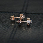 Pair of round halo cluster diamond earrings in gold with center diamonds and surrounding diamond halo, placed on a black surface.