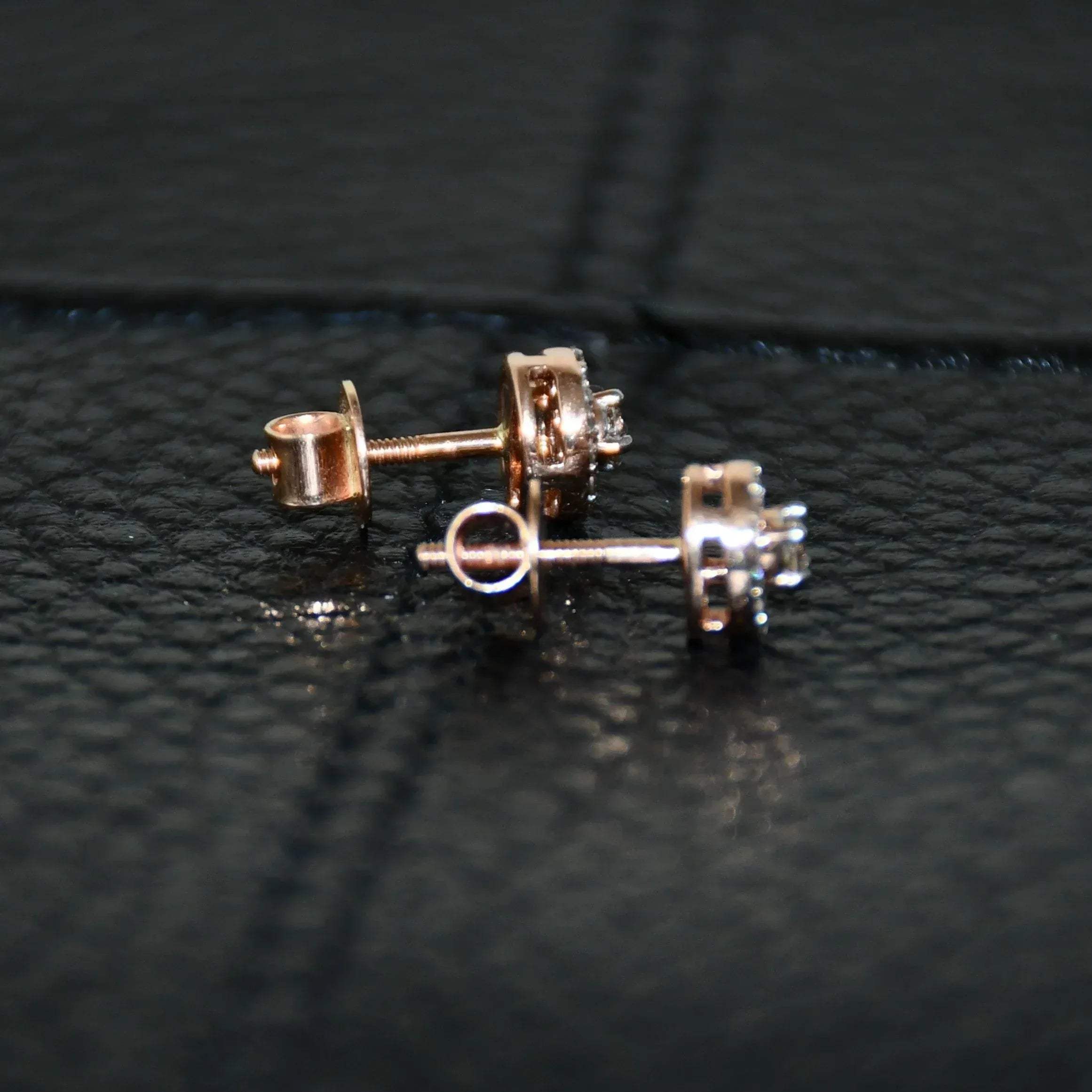 Pair of round halo cluster diamond earrings in gold with center diamonds and surrounding diamond halo, placed on a black surface.