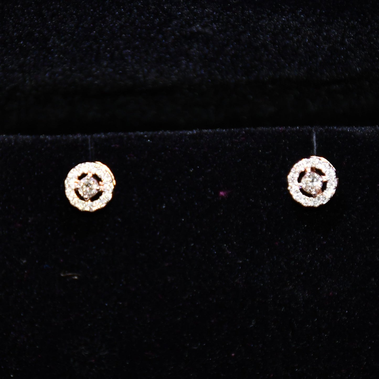 Pair of round halo cluster diamond earrings in gold with center diamonds and surrounding diamond halo, placed against a black background.