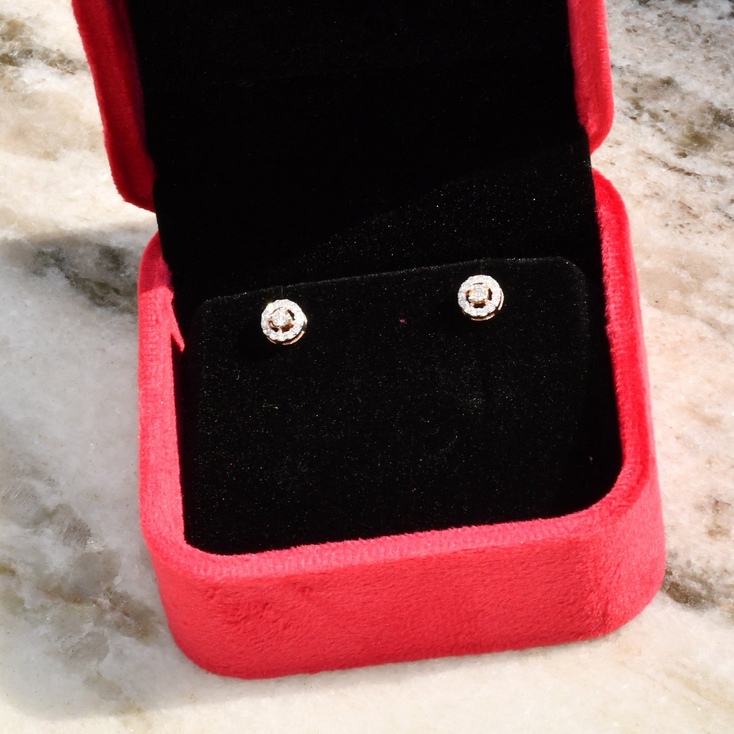 Pair of round halo cluster diamond earrings in gold with center diamonds and surrounding diamond halo, placed in a jewelry box.