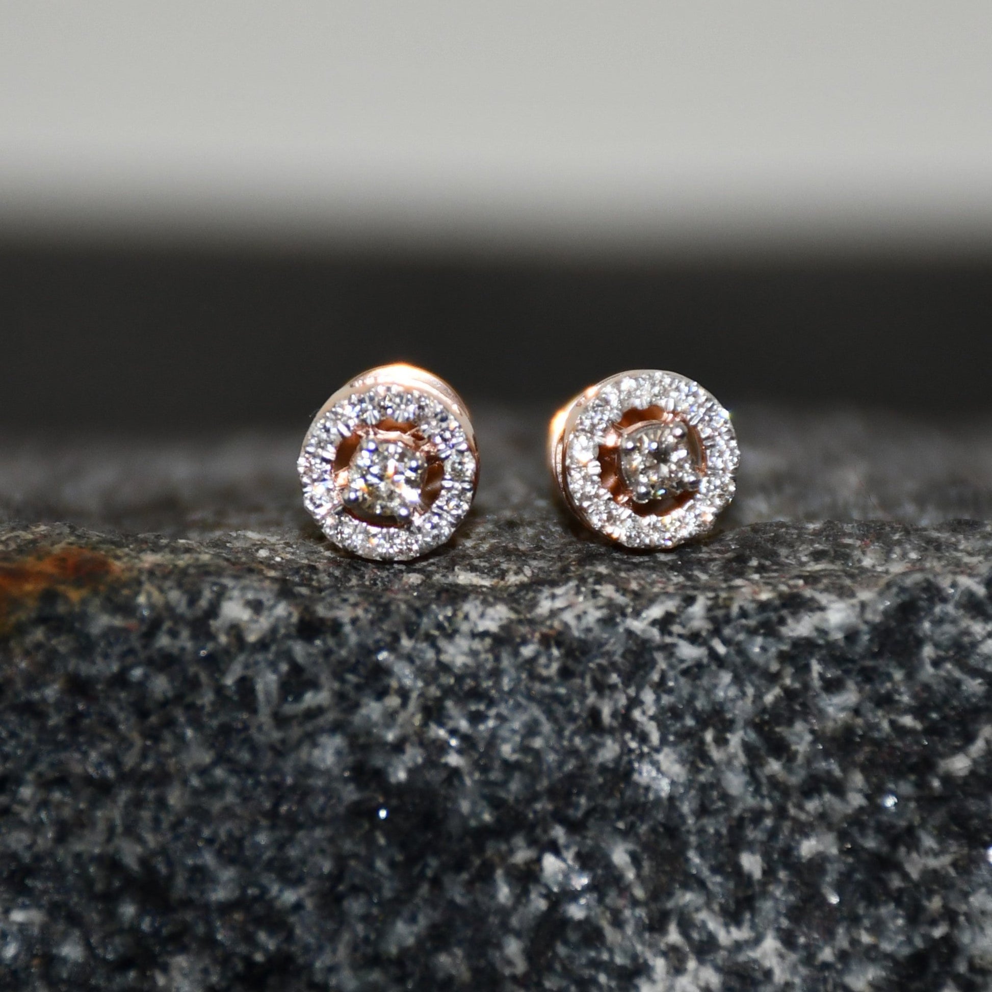 Pair of round halo cluster diamond earrings in gold with center diamonds and surrounding diamond halo, placed on a textured stone surface.