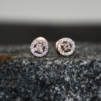 Pair of round halo cluster diamond earrings in gold with center diamonds and surrounding diamond halo, placed on a textured stone surface.