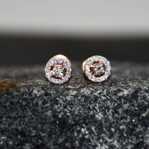 Pair of round halo cluster diamond earrings in gold with center diamonds and surrounding diamond halo, placed on a textured stone surface.