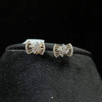 A pair of gold diamond earrings with a round cut design on a mannequin stand.