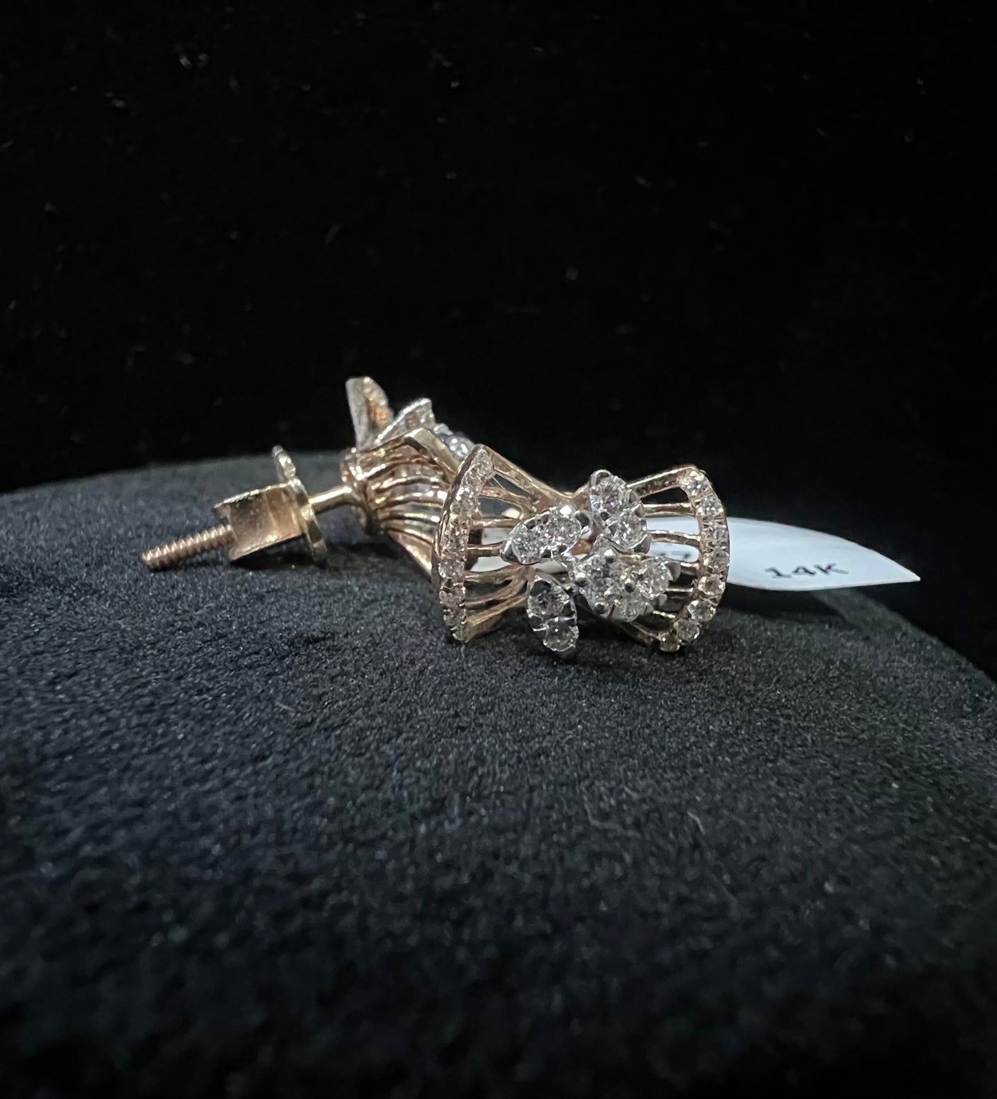 A pair of gold diamond earrings with a round cut design on a mannequin stand.