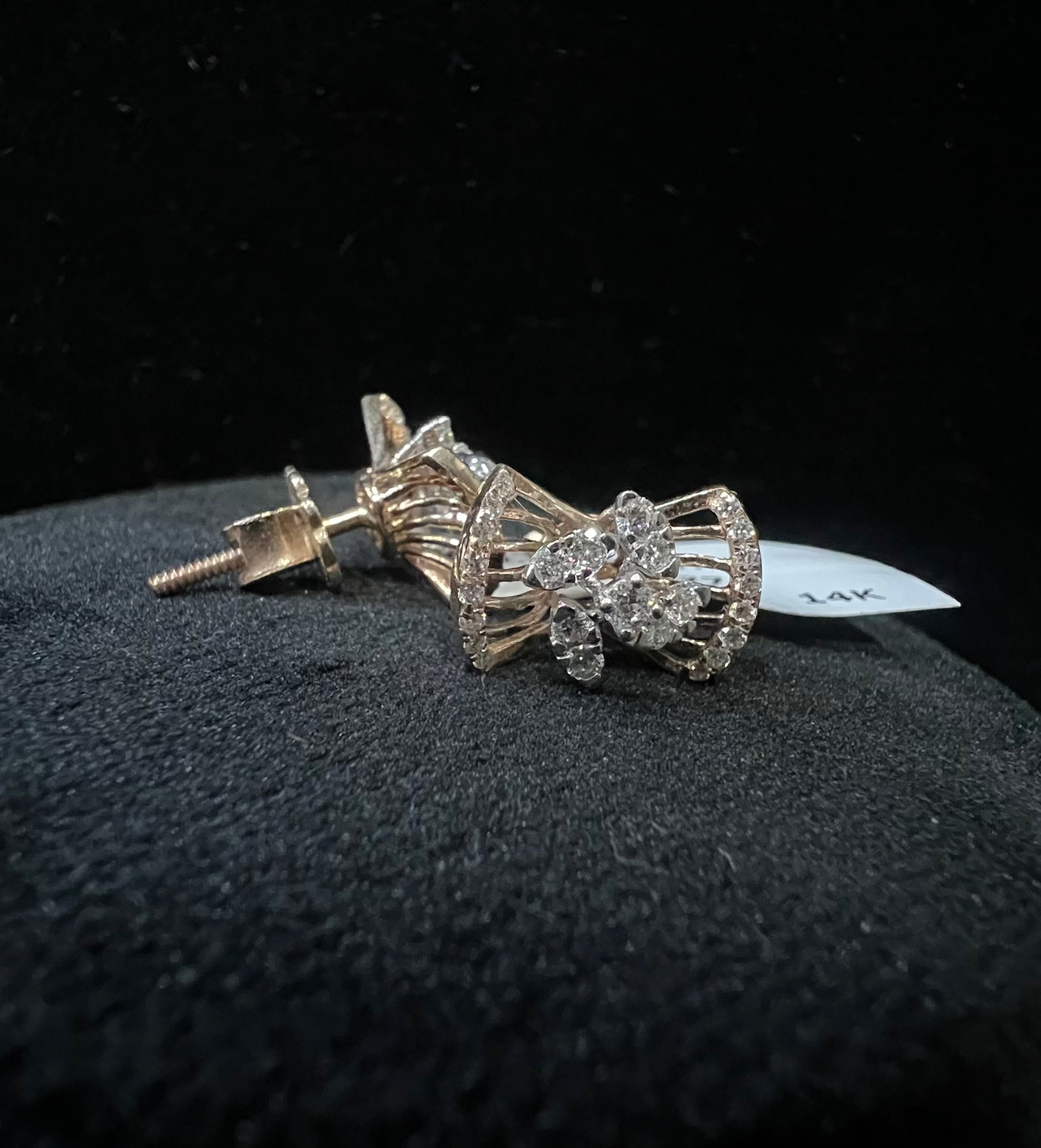 A pair of gold diamond earrings with a round cut design on a mannequin stand.