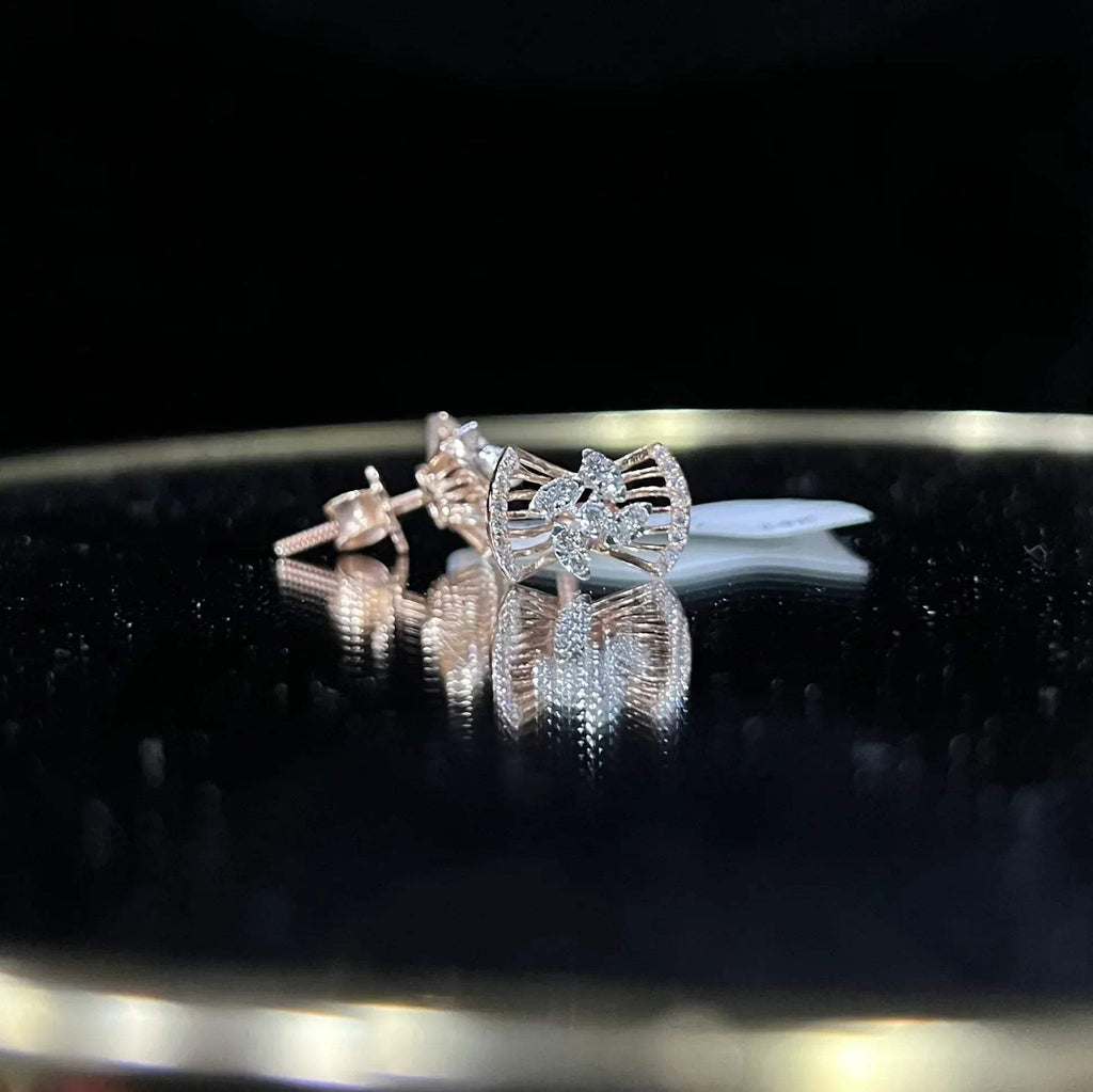 A pair of gold diamond earrings with a round cut design on a reflective surface.