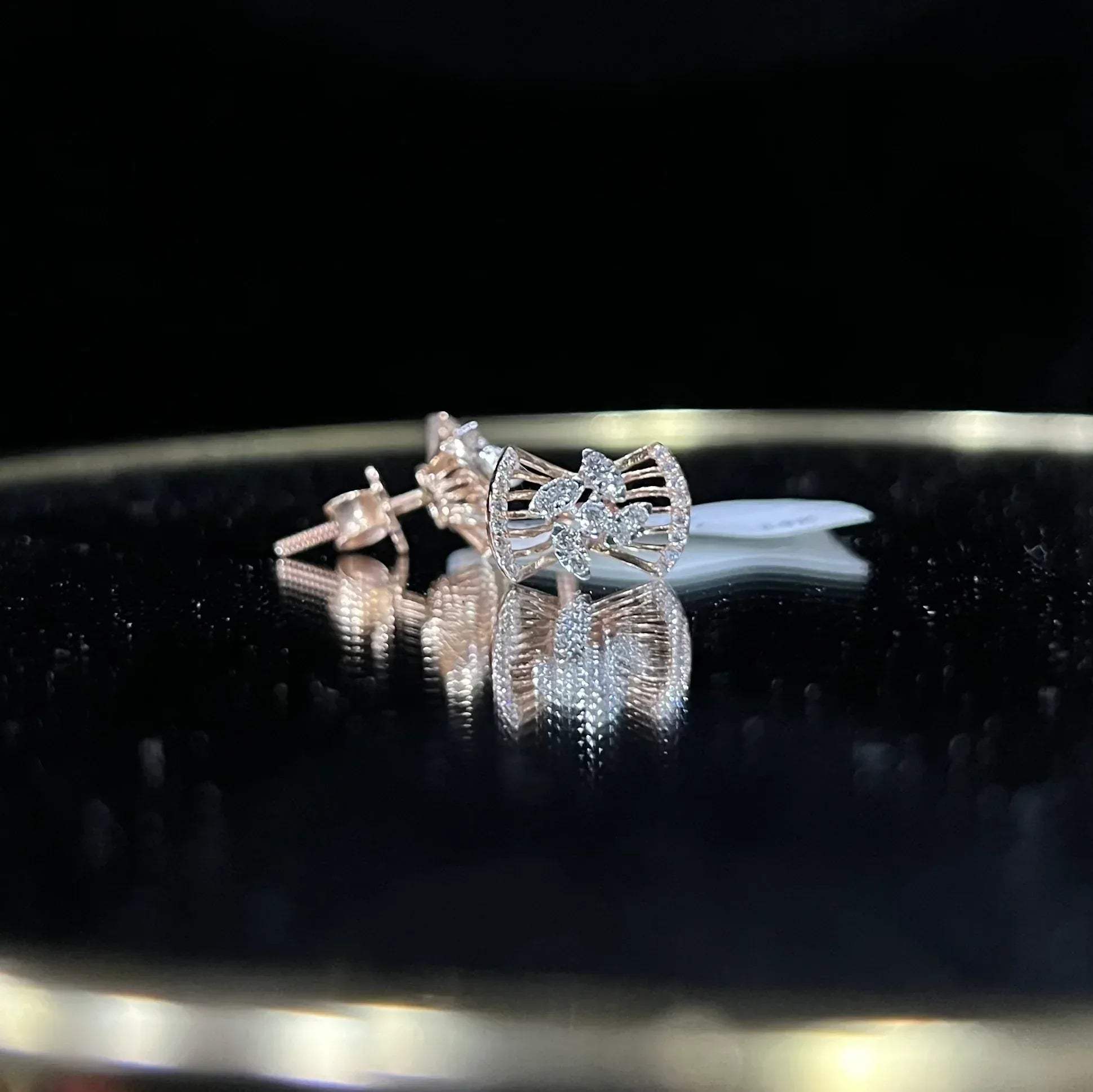 A pair of gold diamond earrings with a round cut design on a reflective surface.