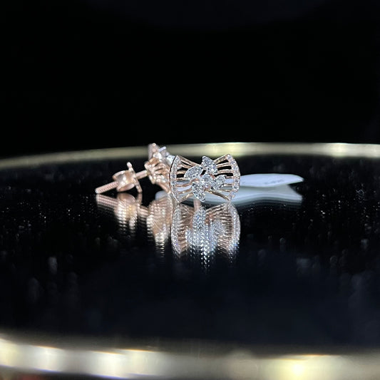 A pair of gold diamond earrings with a round cut design on a reflective surface.