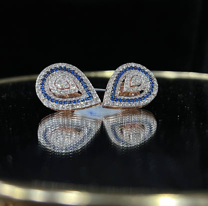 A pair of gold diamond earrings with a geometric pattern, displayed on a reflective surface.