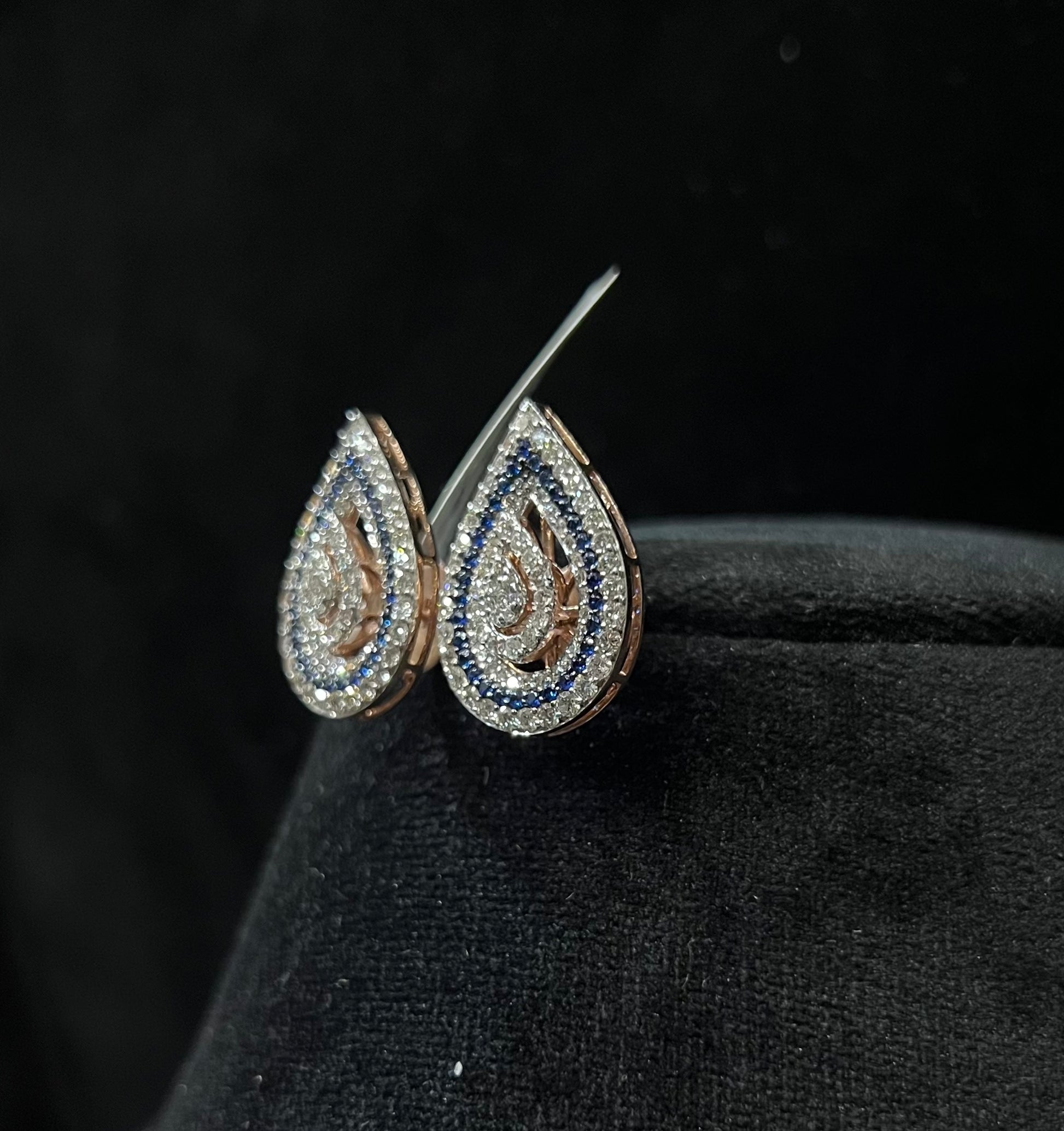 A pair of gold diamond earrings with a geometric pattern, displayed on a mannequin bust.