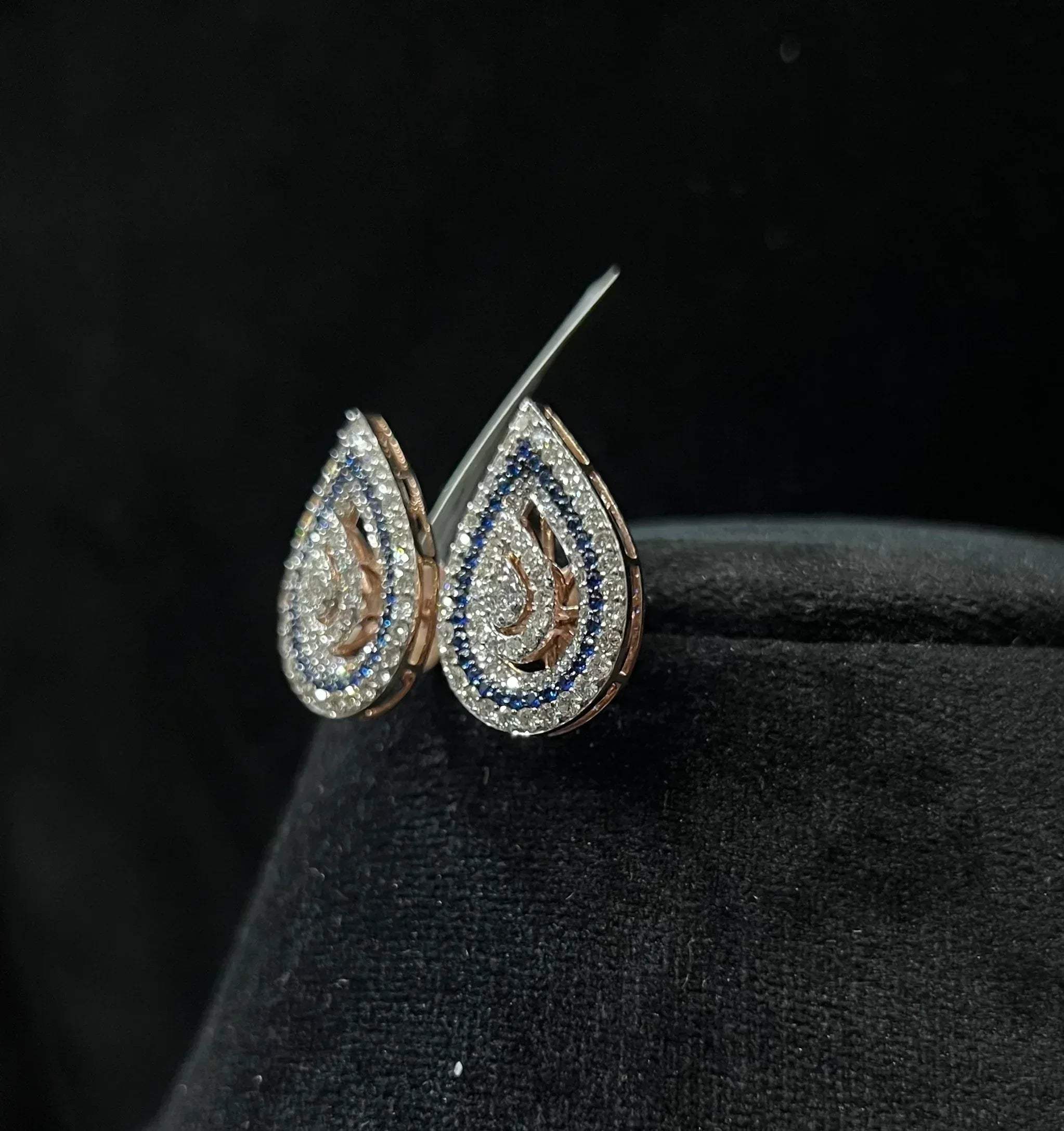 A pair of gold diamond earrings with a geometric pattern, displayed on a mannequin bust.
