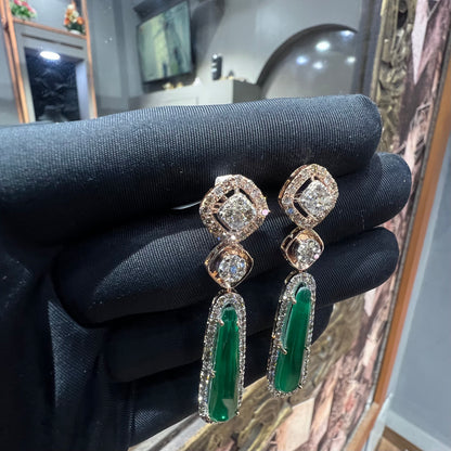 A pair of gold diamond earrings with green color stones set in a minimalist design.