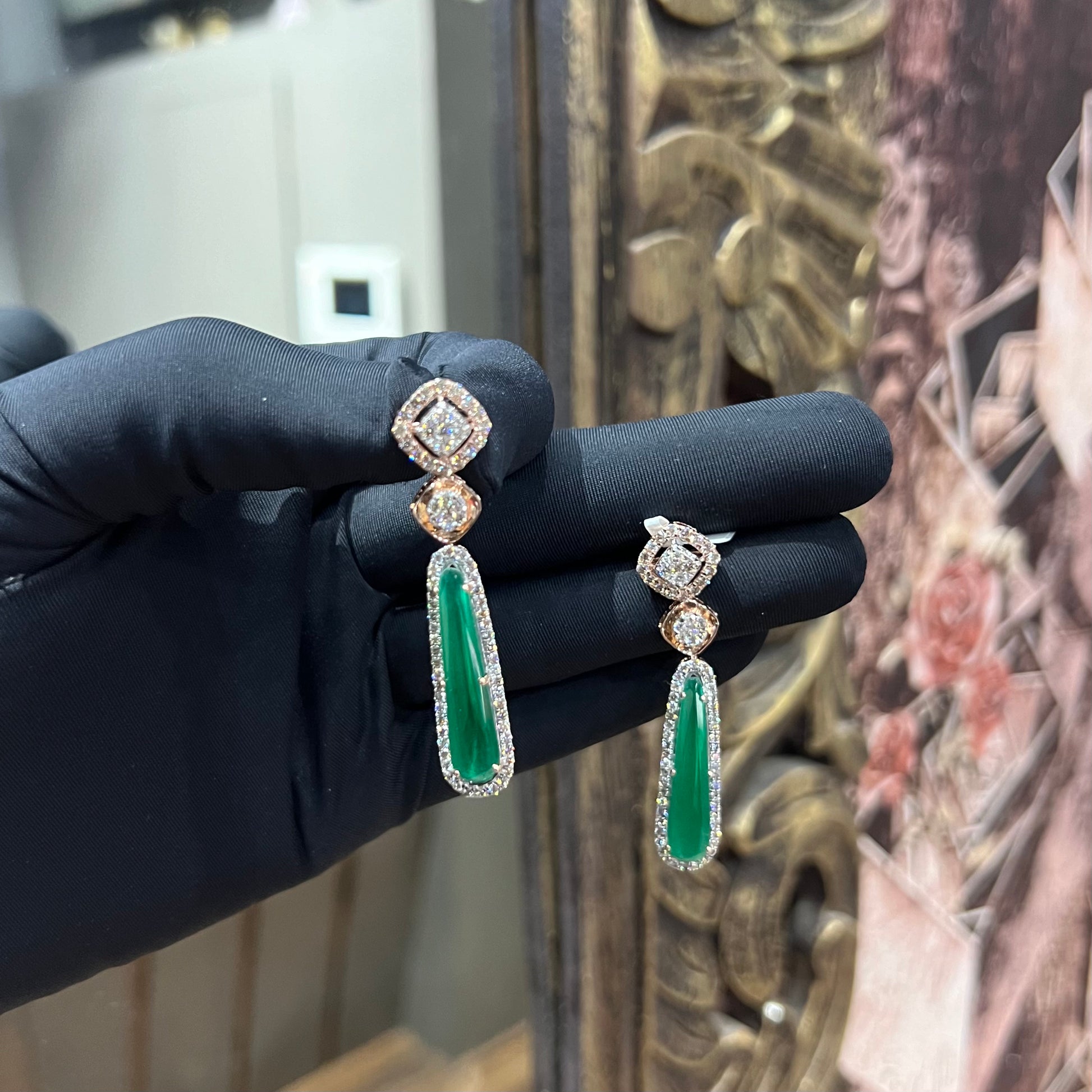 A pair of gold diamond earrings with green color stones set in a minimalist design.