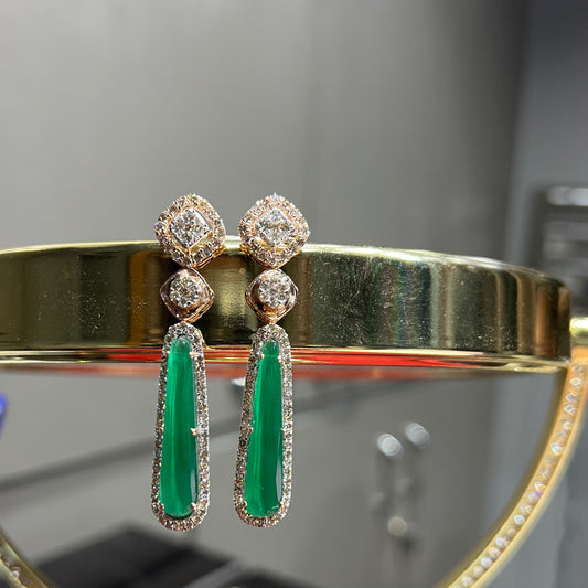 A pair of gold diamond earrings with green color stones set in a minimalist design.