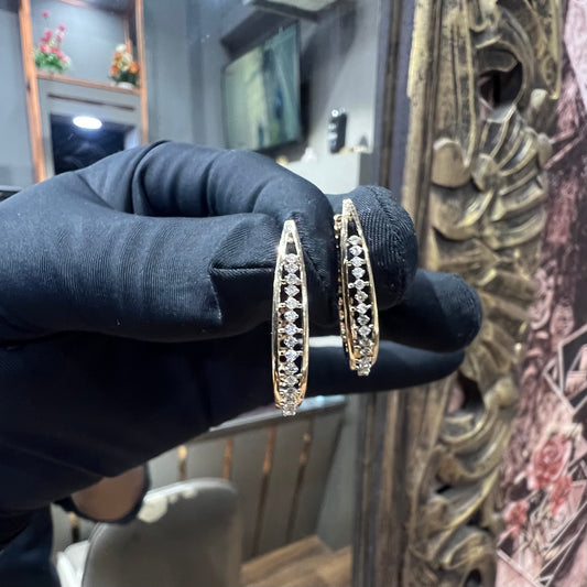 A pair of round-cut diamond earrings held in a person's hand, with a gold band.