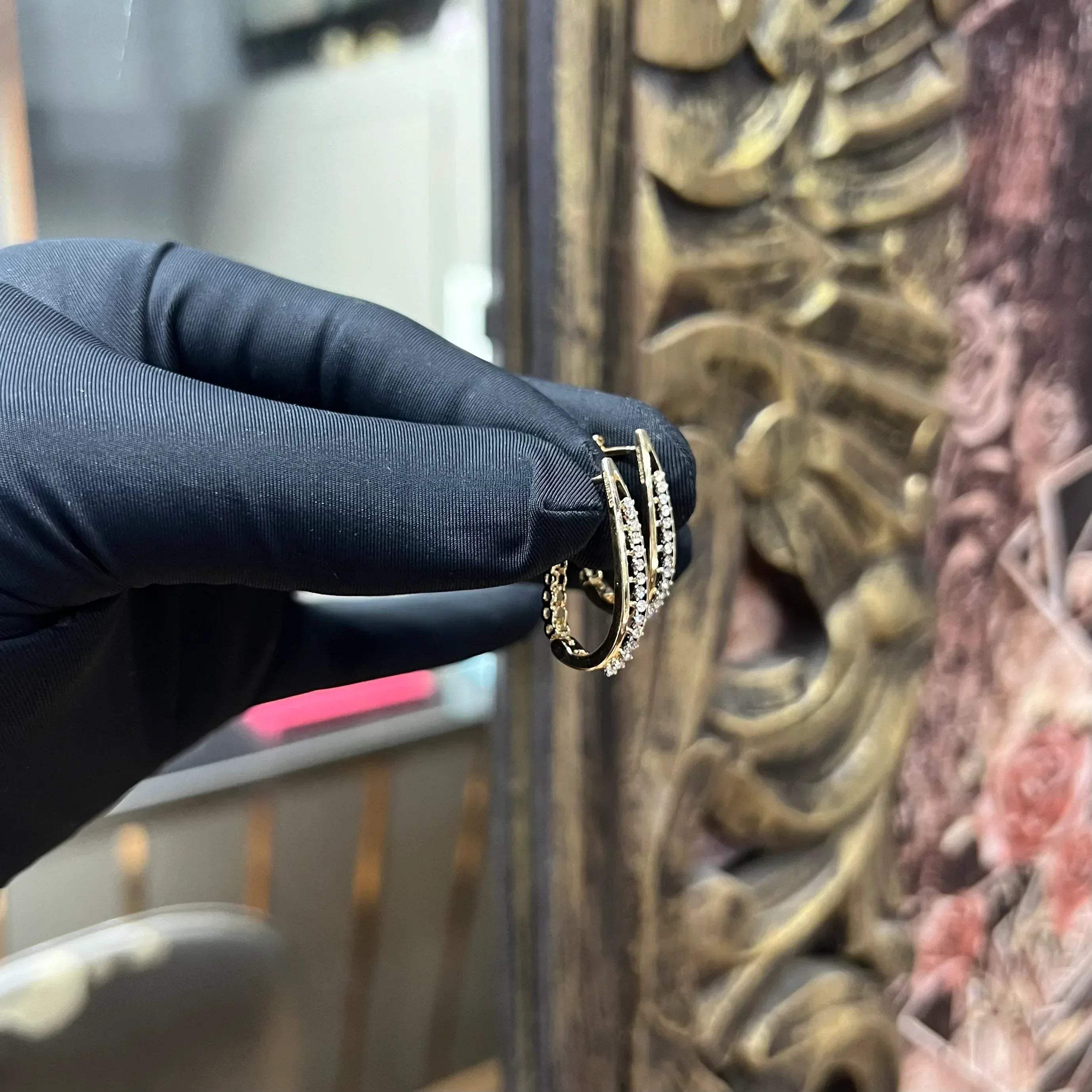 A pair of round-cut diamond hoop earrings held in a person's hand, with a gold band.