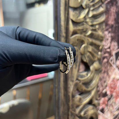 A pair of round-cut diamond hoop earrings held in a person's hand, with a gold band.
