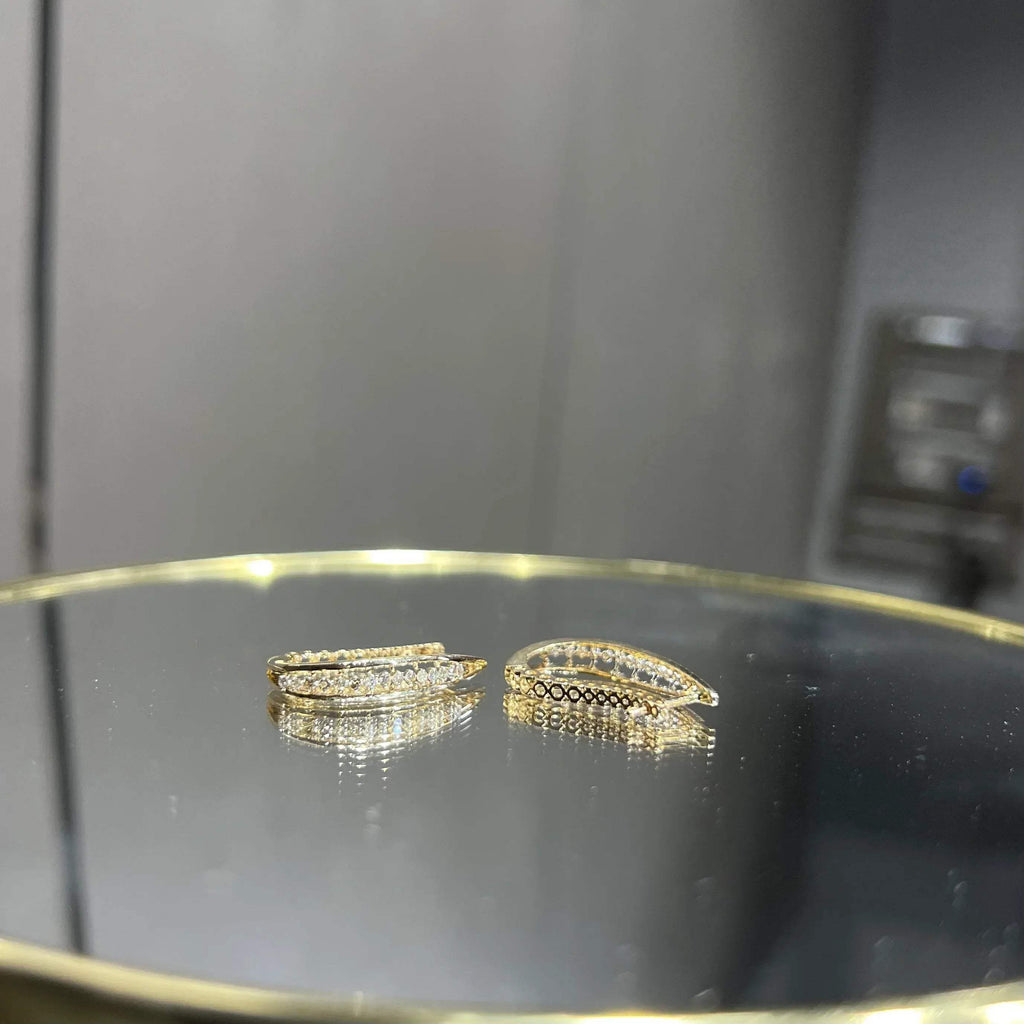 A pair of round-cut diamond hoop earrings held in a person's hand, with a gold band.
