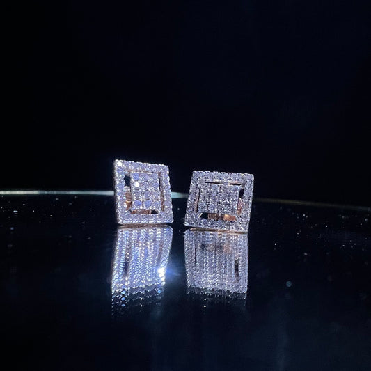 A pair of diamond stud earrings set in a gold casing, displayed against a reflective surface.
